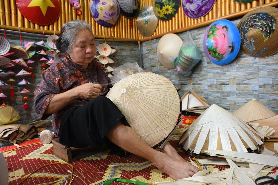 Artisan stitching a conical hat in a hat-making village, Hue
